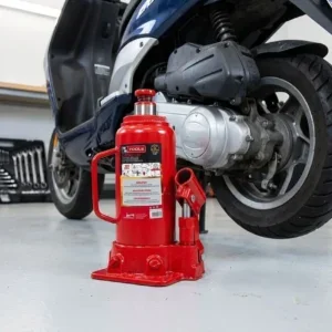 Cric bouteille hydraulique rouge utilisé pour soulever un scooter dans un garage.