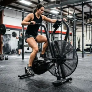 Femme s’exerçant sur un assault bike en salle de sport, pédalant vigoureusement avec les bras sur les poignées.